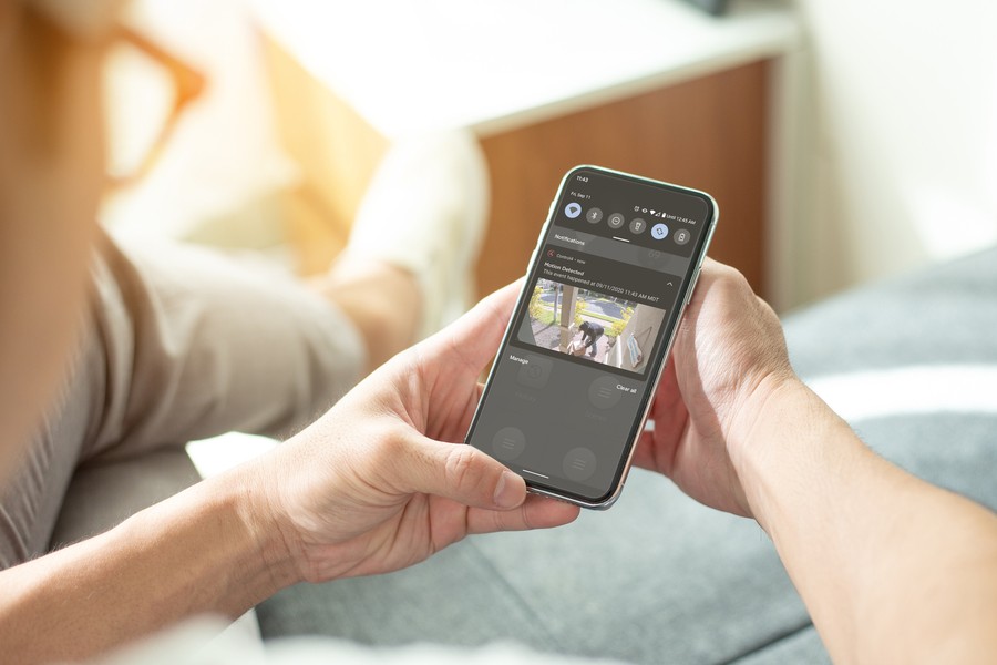 A woman holding a smartphone showing the Control4 app. She is viewing live footage of someone at her front door on the app. 