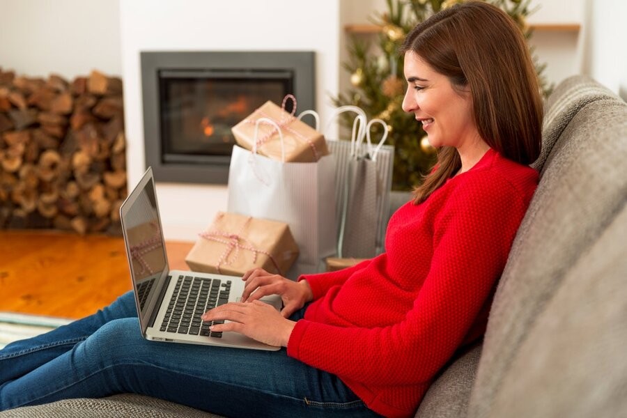 A woman sitting on her couch with a laptop with holiday decorations in the background.