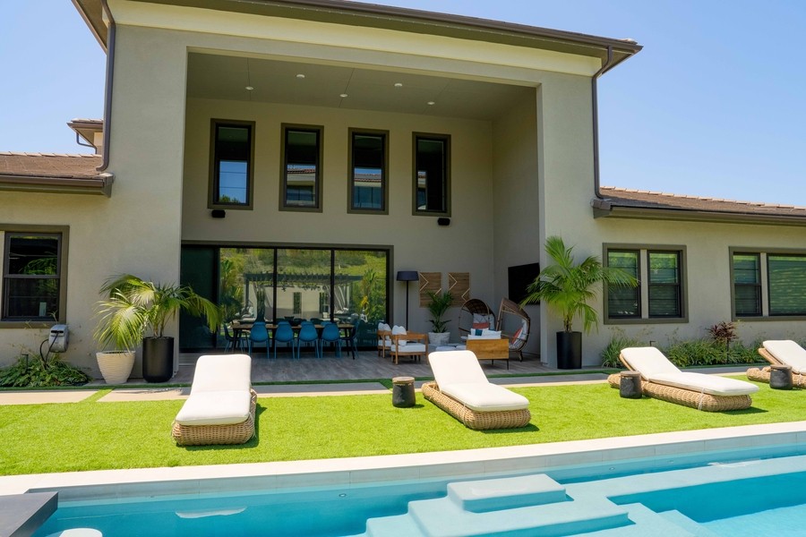 A modern luxury patio with lounging chaises by a large swimming pool.