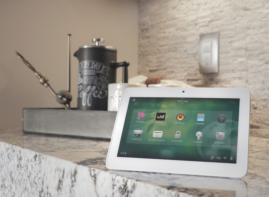 touchscreen tablet showing a Control4 smart home management system, set on top of a counter