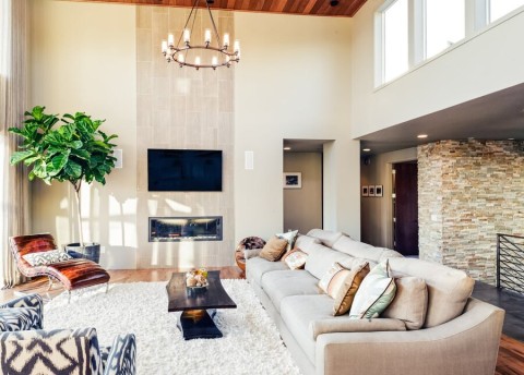 A living space with a high ceiling with a chandelier, a couch, and flat-screen TV on the wall.