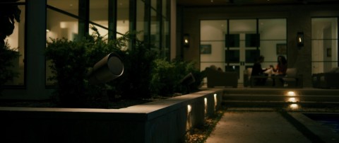 outdoor speaker in a landscaping flower bed with a couple sitting in the background