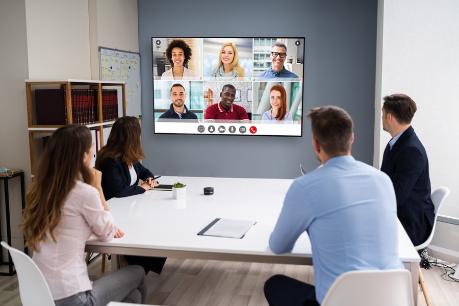 employees sitting around a conference table looking at a video conference screen at the front of the room