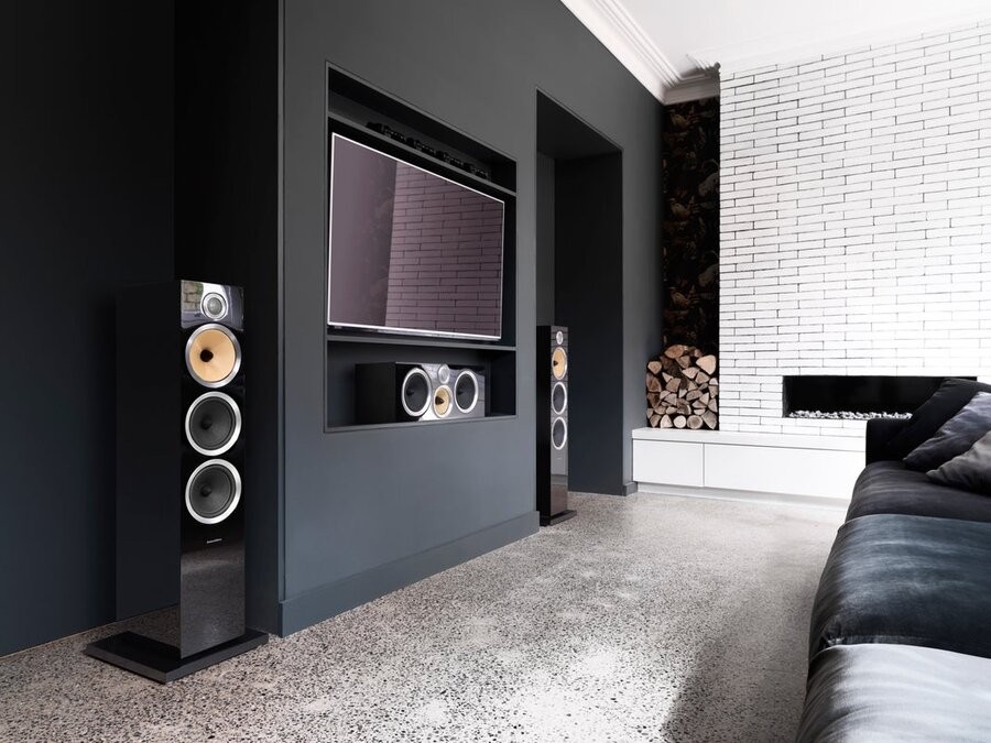 A media room space featuring a screen and couch with two Bowers & Wilkins standing speakers on either side of the TV cabinet.