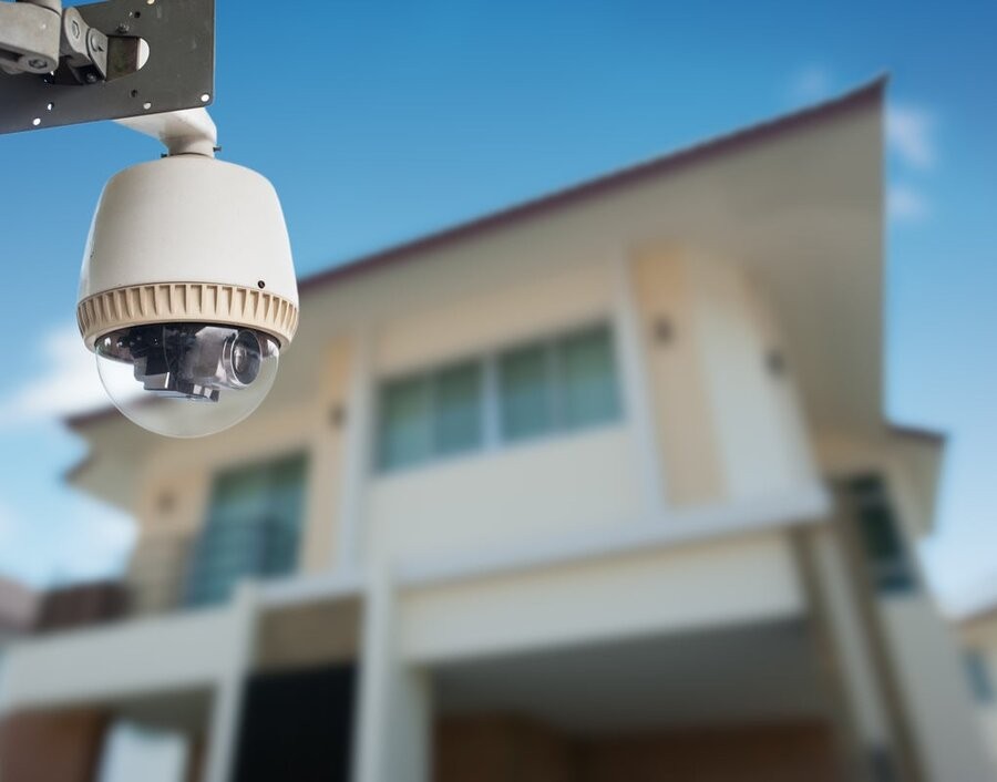 A smart surveillance camera in focus with a home’s exterior in the background.